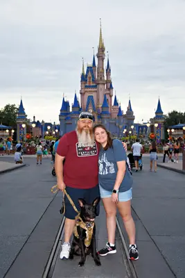 Erica, her husband, and their service dog in front of Cinderella Castle